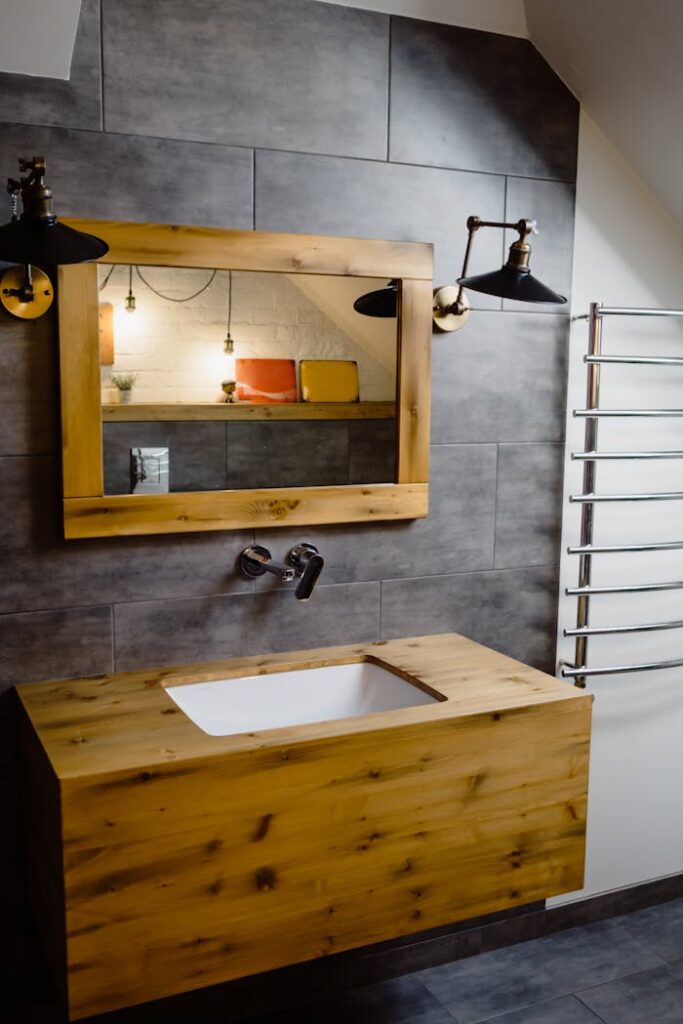 pexels-photo-5644328 Modern bathroom featuring a wooden vanity, large mirror, industrial lamps, and a sleek gray tile wall.